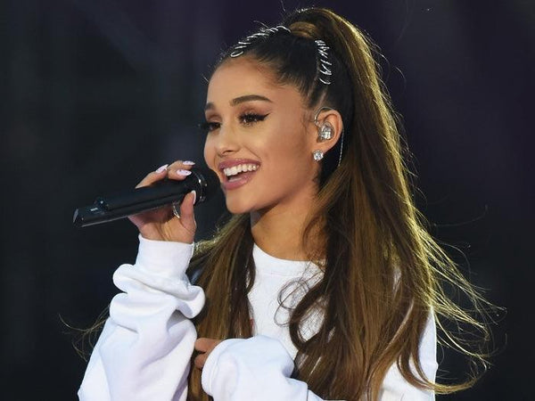 Smiling woman with long brown hair in a white sweatshirt singing on stage with microphone