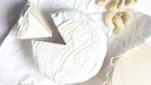 Dairy-free cheese wheel with a slice cut out and cashews on white parchment paper