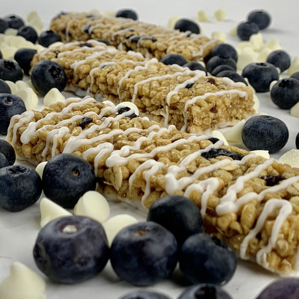 Nut-free blueberry vanilla snack bars with white drizzle, surrounded by fresh blueberries and white chips