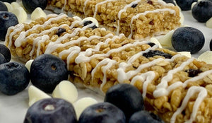 Nut-free blueberry vanilla snack bars with white icing, surrounded by blueberries and white chocolate chips