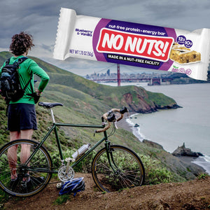 No Nuts nut-free snack bar with blueberry vanilla flavor above mountain biker overlooking Golden Gate Bridge