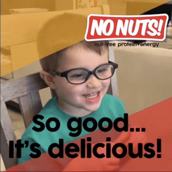 Smiling child with glasses enjoying No Nuts nut-free snack bar, text reads 'So good... It's delicious!'