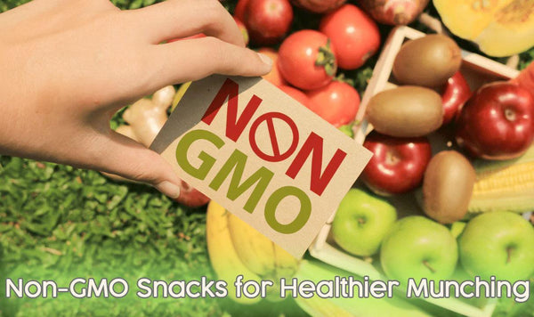 Hand holding a non-GMO sign above fresh fruits and vegetables, healthy snack concept.