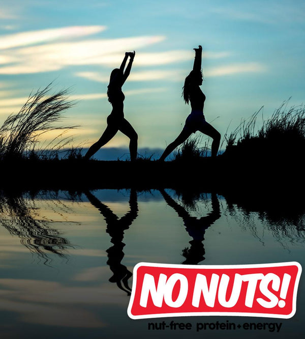 Two people doing yoga by a lake at sunset, No Nuts! nut-free snack bars logo in foreground.