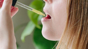 Person using dropper to take allergy-friendly liquid supplement, green plant in background.