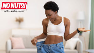 Happy woman in white top celebrating weight loss with loose jeans, No Nuts nut-free snack bar logo visible.