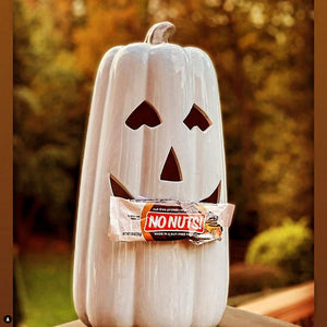 Nut-free No Nuts snack bar held by a white ceramic jack-o'-lantern outdoors in autumn light.