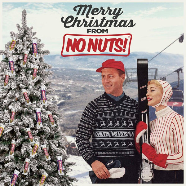 Vintage Christmas scene with a couple in ski gear, snowy tree decorated with No Nuts snack bars, and Merry Christmas from No Nuts sign.