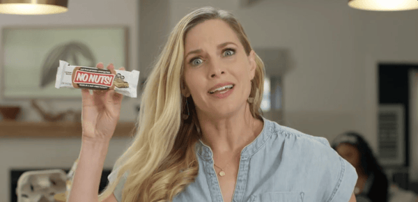 Woman holding No Nuts nut-free snack bar in kitchen, allergy-friendly school-safe snack