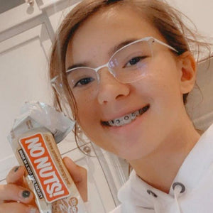Smiling girl with braces holding a No Nuts nut-free snack bar in a kitchen