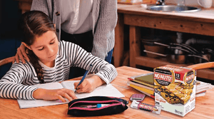 Student doing homework at table with No Nuts nut-free snack bars, books, and school supplies