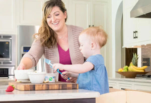 Smiling woman and child preparing nut-free snack in a bright kitchen with fruit in background