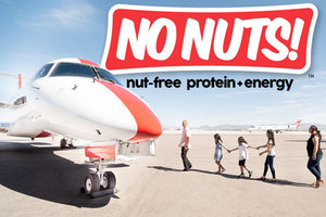 Family walks on airport tarmac by jet with No Nuts! nut-free snack bars logo above.