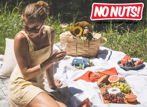 Woman enjoying nut-free picnic outdoors with fruit, cheese, and No Nuts! snack bars.