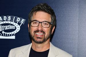 Smiling man with glasses and beard at Roadside Attractions event, nut-free snack bar theme