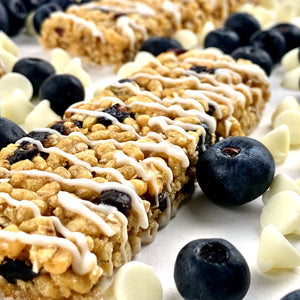 No Nuts blueberry vanilla protein snack bar with white vanilla drizzle, fresh blueberries, and white chips.